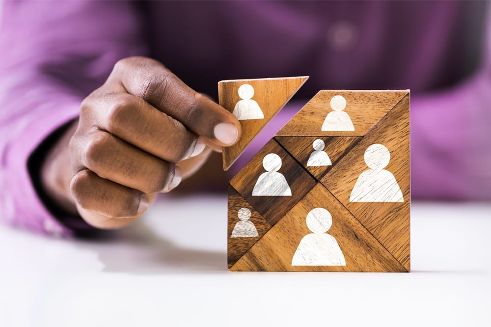 Image shows hand using building blocks. Each block has an icon representing a human to signify team building.