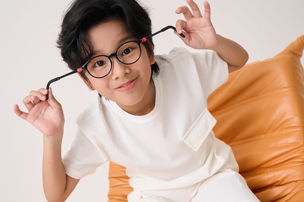 Image shows child in glasses. He's pulling on the frames to show how flexible they are.