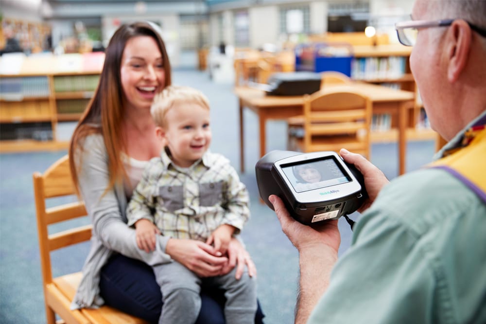 child sitting on mother's lap, being tested with spot vision screener
