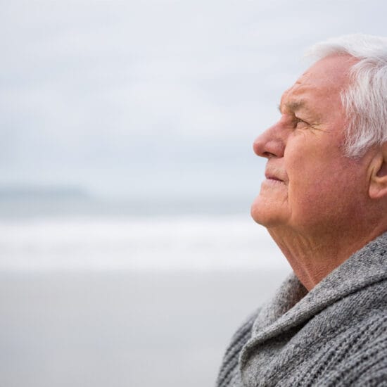 Older man standing at the beach in thought. Glaucoma care outside the consulting room can help with emotions of glaucoma diagnosis.