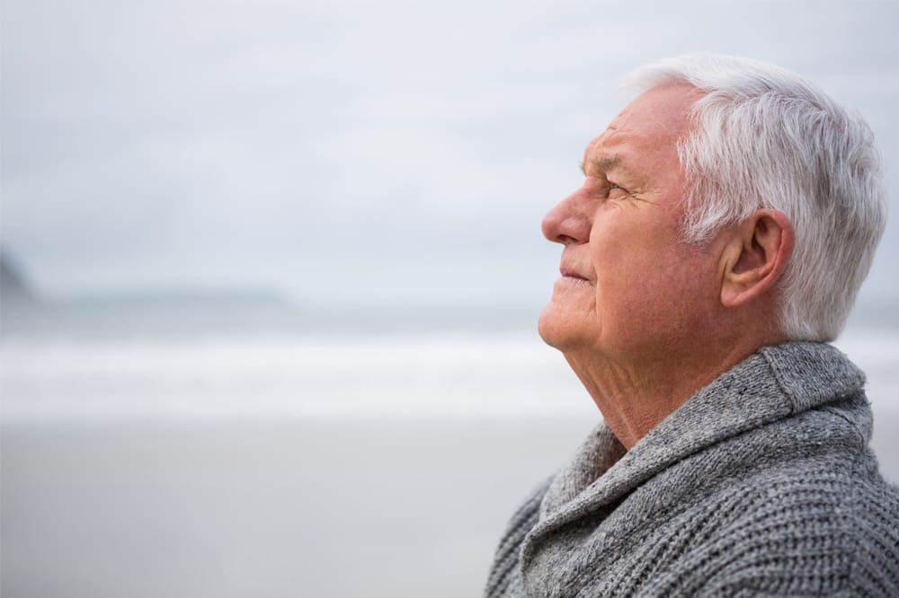 Older man standing at the beach in thought. Glaucoma care outside the consulting room can help with emotions of glaucoma diagnosis.