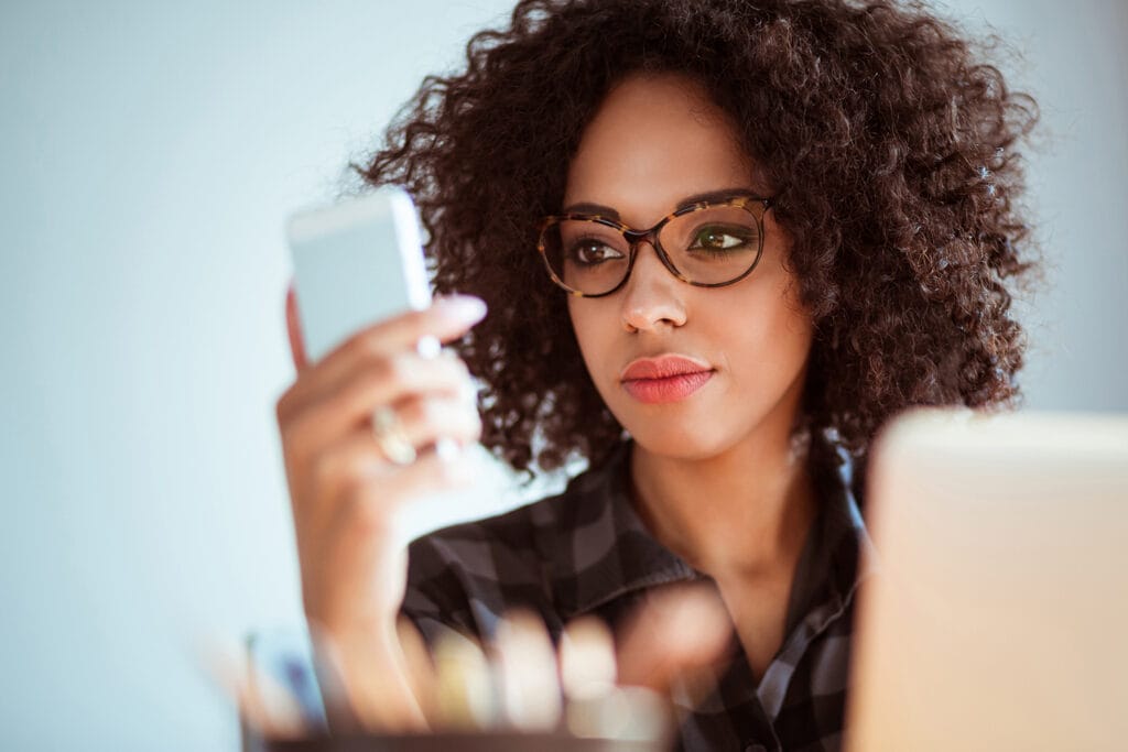 Close up of young african woman wearing Shamir occupational lenses and reading text message on her mobile phone at office 