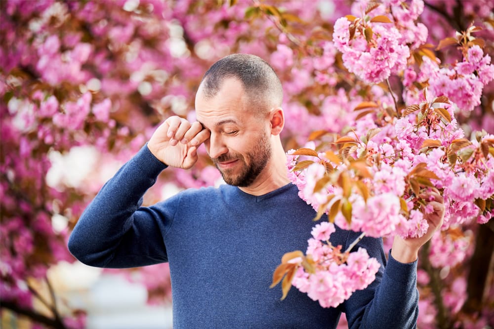 man with itchy eyes surrounded by blossoms