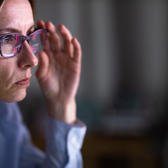 Image shows a woman with glasses staring at a screen.